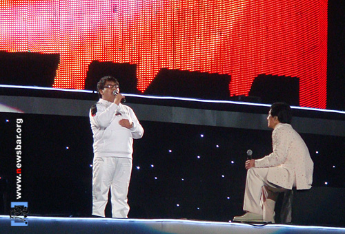 成龙慈善演唱会，成龙(右)坐在音箱上听盲人歌手唱歌。